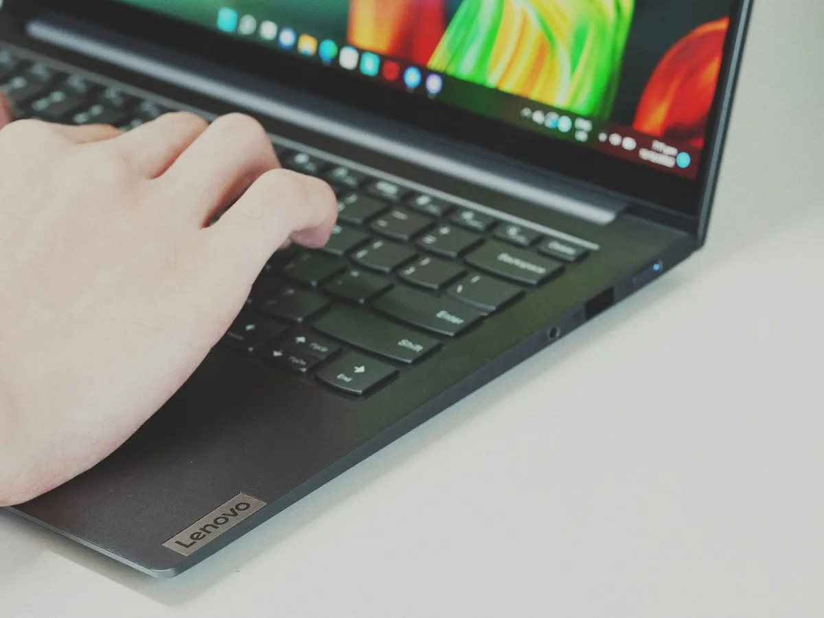 Mãos digitando em um notebook Lenovo aberto